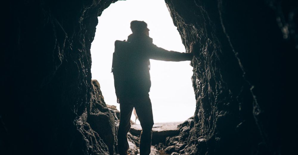 New Terrain Rock Climbing - A silhouette of a hiker exploring a dark cave with light in the background, symbolizing adventure and discovery.