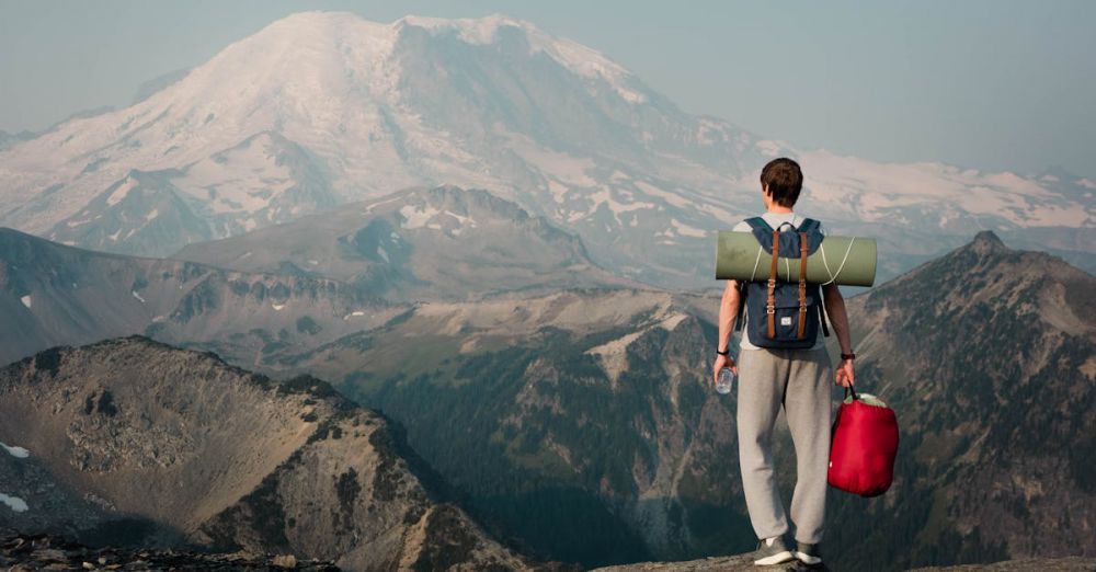 High-Altitude Rock Climbing - Backpacker on a mountain ridge gazing at a snow-covered peak, embracing adventure.