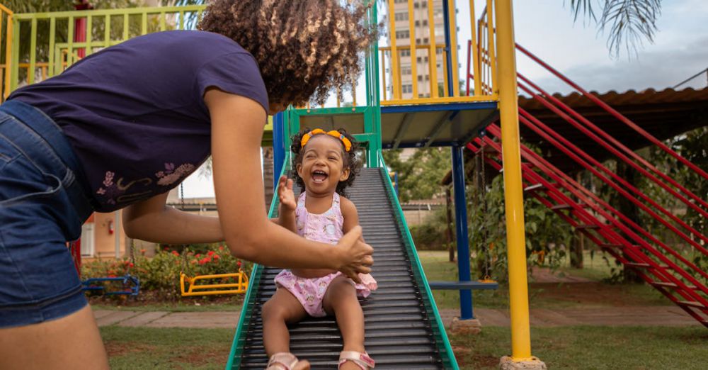 Children’s Urban Gardens - Happy mother and daughter enjoying time at an outdoor playground slide.