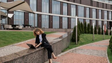 Relaxation Urban Gardens - A woman in a black coat works on her laptop outside a modern building.