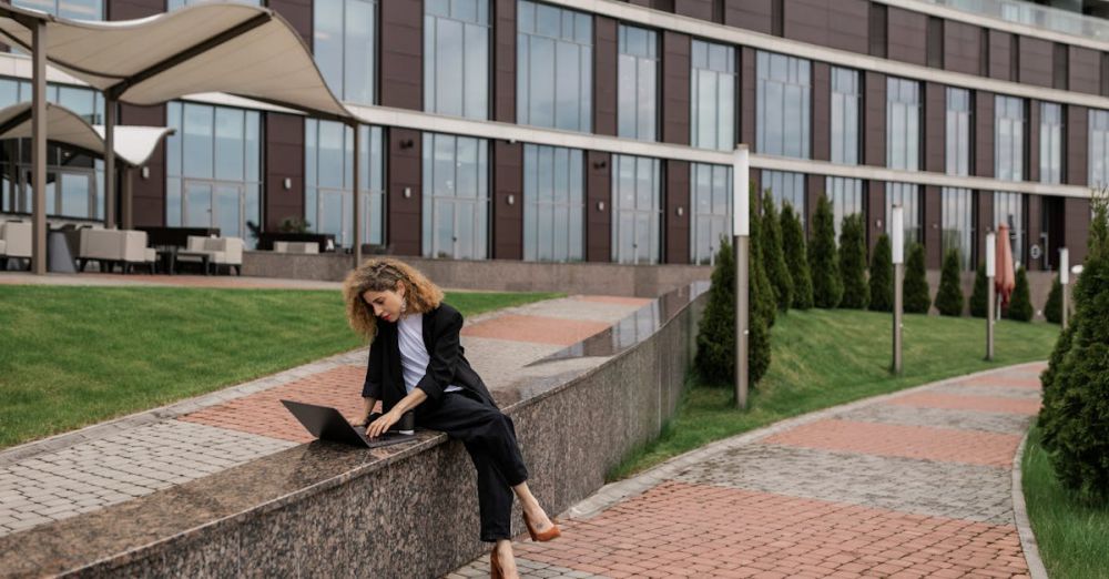 Relaxation Urban Gardens - A woman in a black coat works on her laptop outside a modern building.