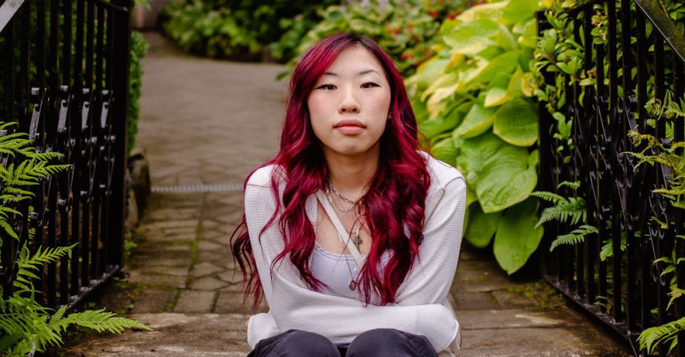 Meditative Urban Gardens - Portrait of a woman with long dyed hair sitting on stone stairs surrounded by lush greenery.