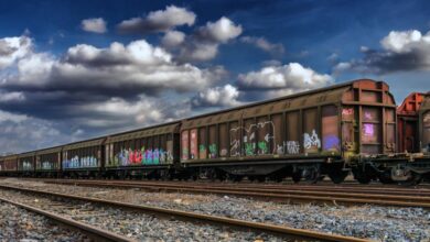 Goods - Freight train in a railway yard with colorful graffiti under a cloudy sky.