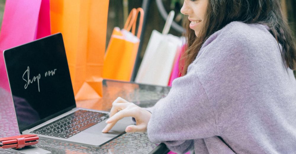 Bargains - A woman shops online using a laptop outdoors, surrounded by colorful shopping bags, representing modern retail therapy.