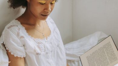 Books - A young woman with natural hair enjoys reading a book by the window with warm sunlight.