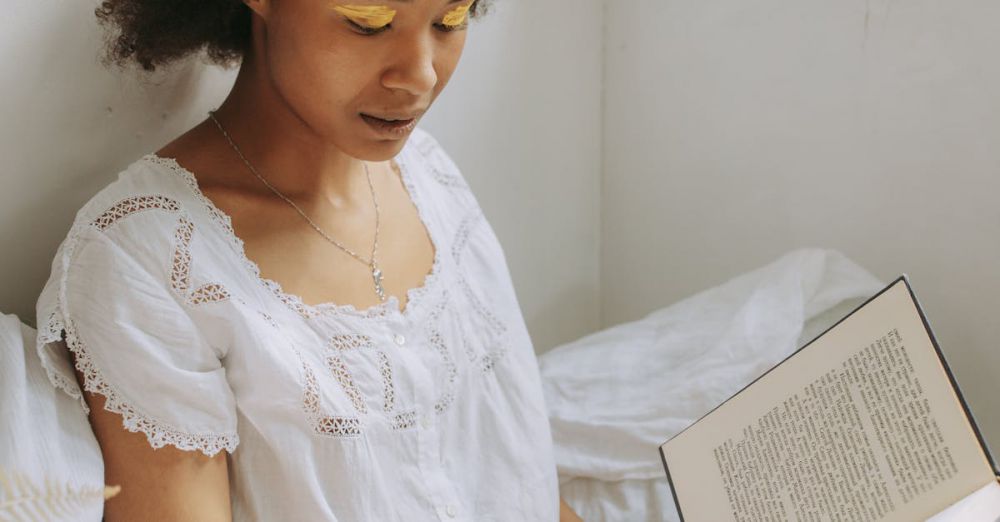 Books - A young woman with natural hair enjoys reading a book by the window with warm sunlight.