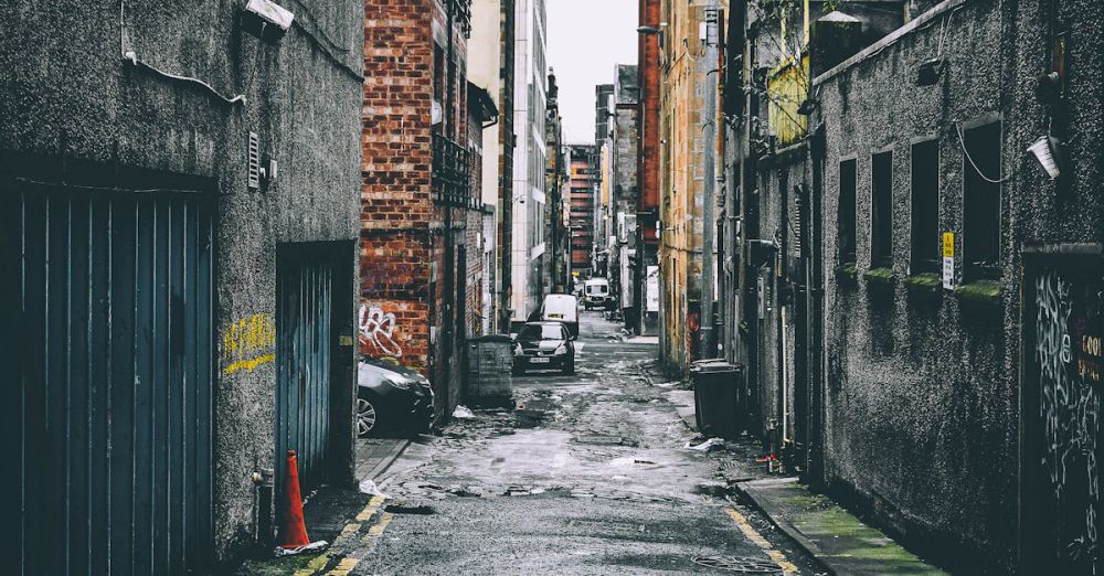 Streets - Quiet urban alley with parked cars between old brick buildings, showcasing city life.