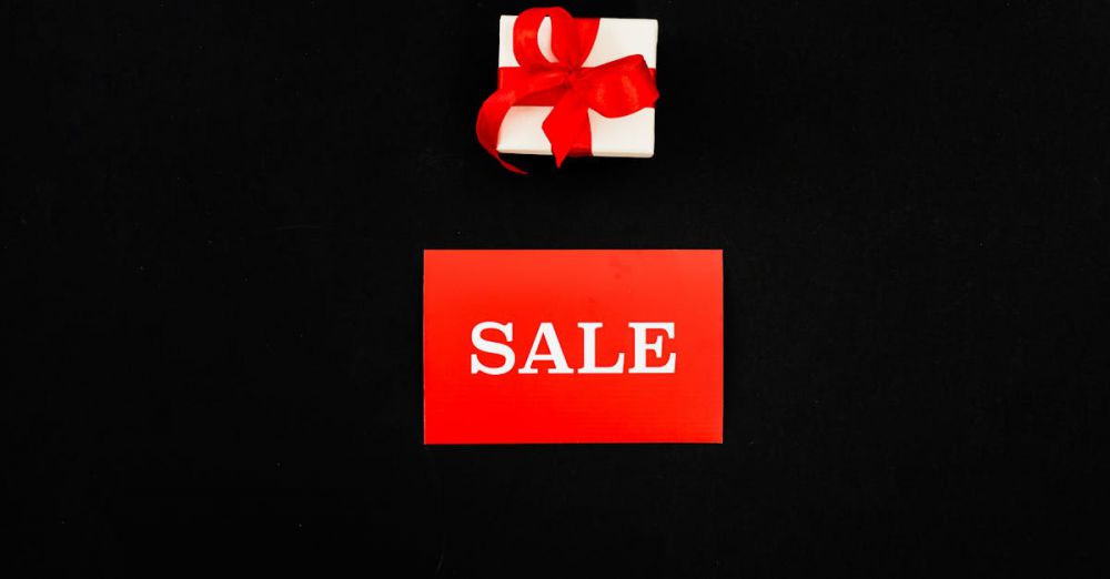 Affordable Gifts - Top view of a red sale card and gift box with a ribbon on a black background. Perfect for shopping promotions.