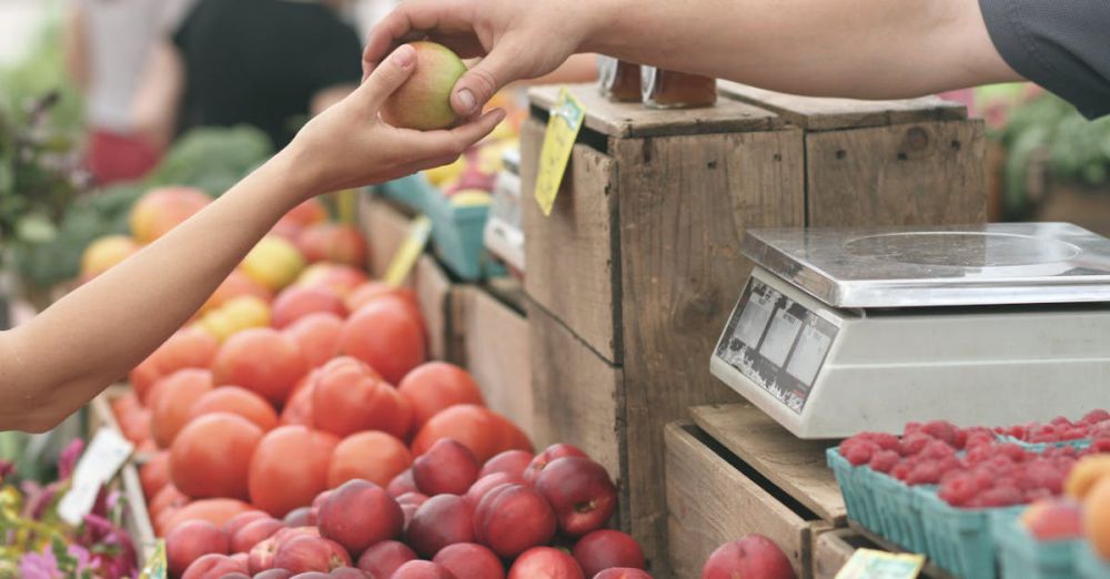 Markets - A customer exchanges an apple with a vendor at a vibrant farmers market.