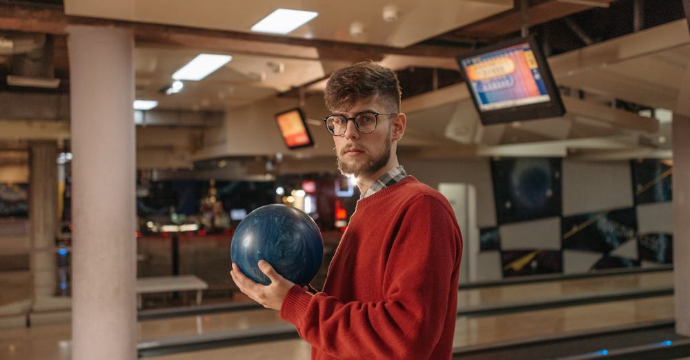 Venues - Young man in a red sweater holding a blue bowling ball in an indoor bowling alley setting.