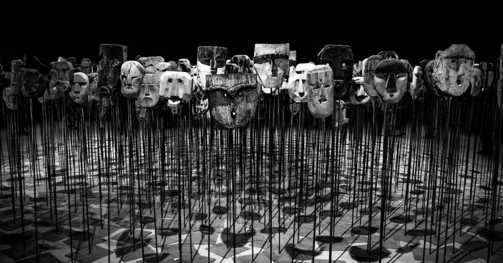 Theater - An artistic display of wooden masks on poles, set in a dimly lit theater.