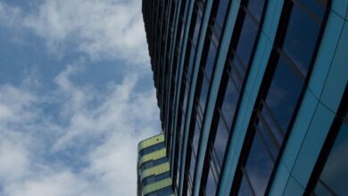 Companies - Low-angle view of modern skyscrapers with reflective windows and cloudy sky backdrop.