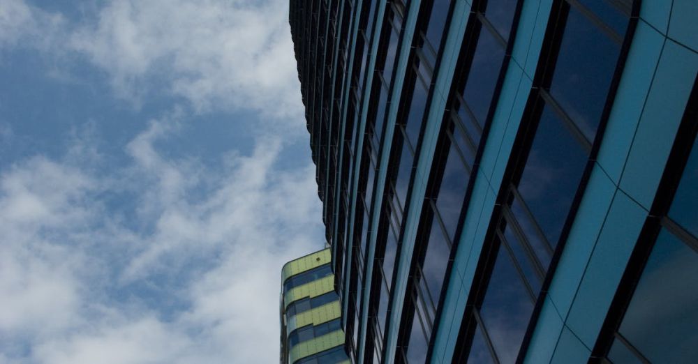 Companies - Low-angle view of modern skyscrapers with reflective windows and cloudy sky backdrop.