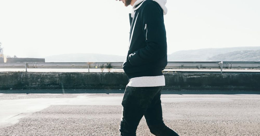 Walking - Casual male in a cap and hoodie walks along a sunny urban street.