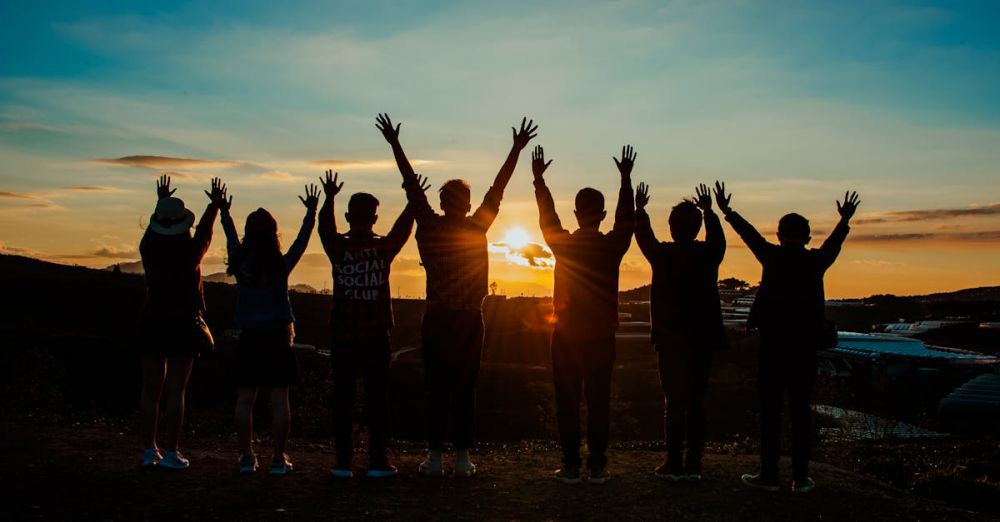 Group - A diverse group of friends raises their arms in celebration against a vibrant sunset backdrop.