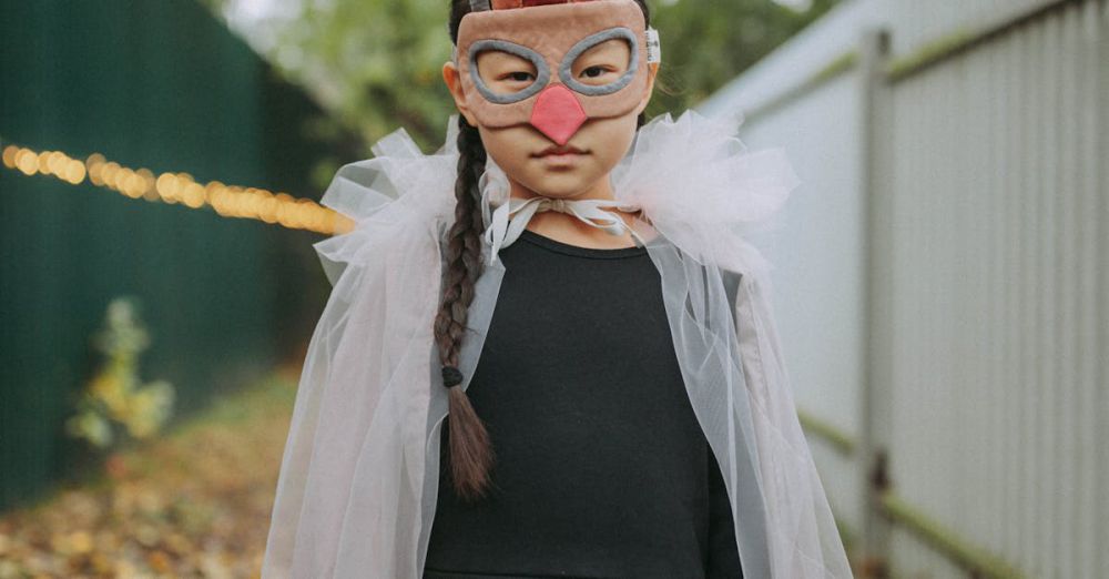 Halloween - A child in a creative costume wearing a mask holds a basket while standing outdoors on a leafy path.