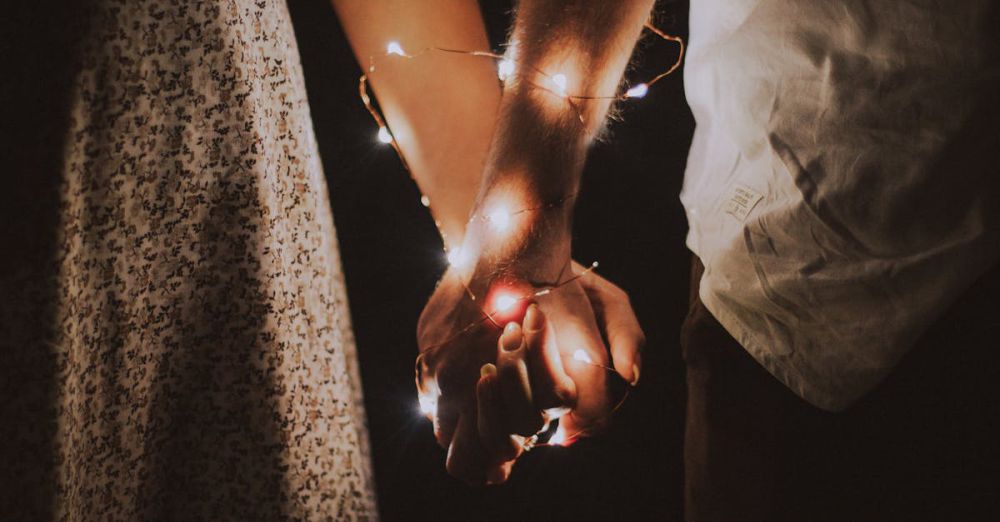 Couples - A warm and intimate close-up of a couple holding hands adorned with glowing string lights.