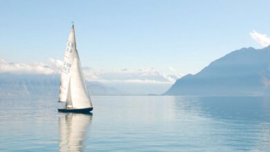 Sailing - Sailing boat glides peacefully on a misty lake surrounded by mountains, under clear daylight.
