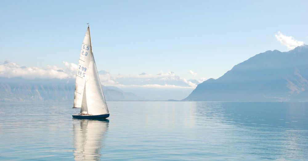 Sailing - Sailing boat glides peacefully on a misty lake surrounded by mountains, under clear daylight.