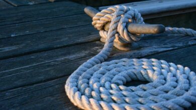 Sailing - Close-up of a sturdy nautical knot on a weathered wooden dock at sunset.