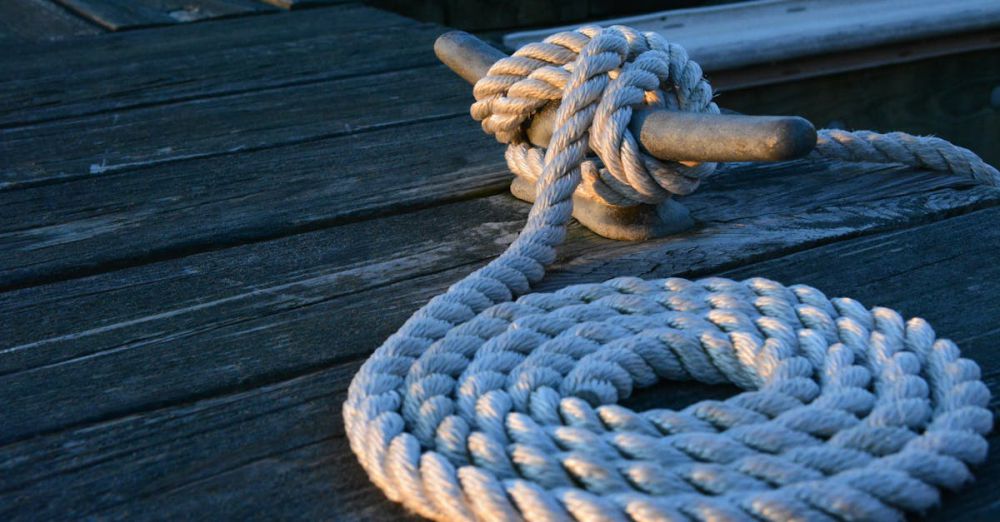 Sailing - Close-up of a sturdy nautical knot on a weathered wooden dock at sunset.