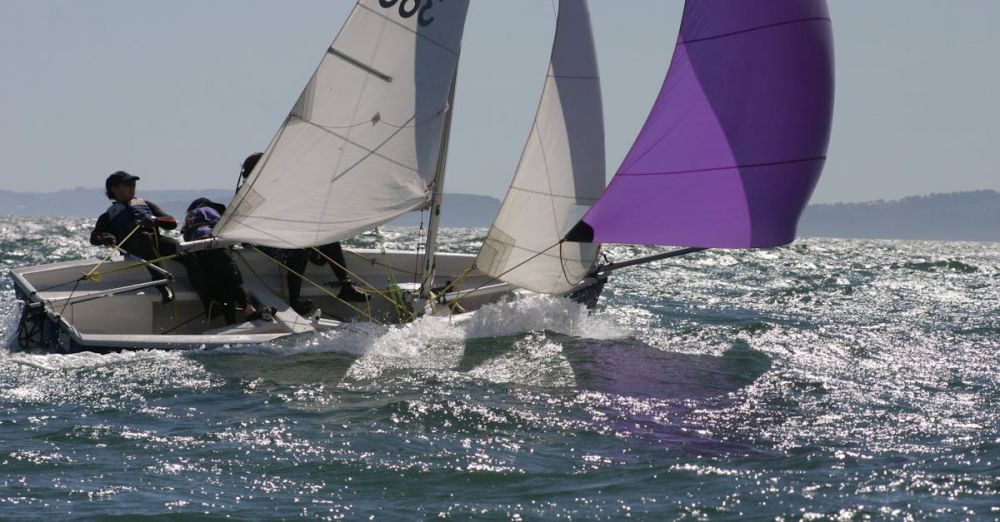 Sailing - Two sailors navigate a sailboat with colorful spinnaker on a sunny ocean day.