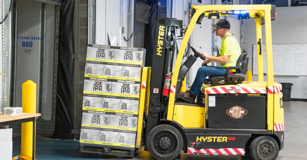 Safety - A worker drives a Hyster forklift moving Joe IPA boxes in a warehouse.