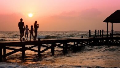 Family - Silhouetted family enjoys a stroll on the beach pier at a vibrant sunset over the ocean waves.