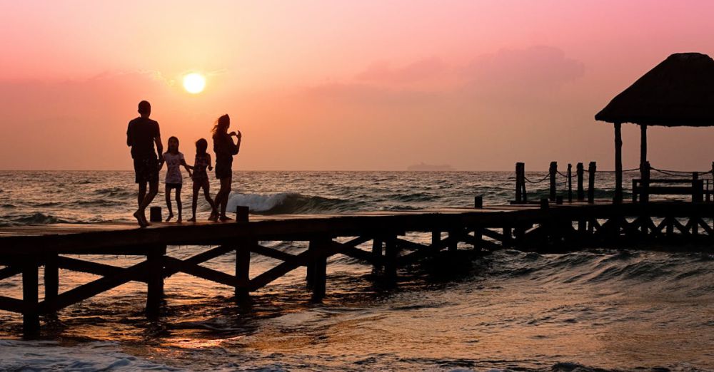 Family - Silhouetted family enjoys a stroll on the beach pier at a vibrant sunset over the ocean waves.