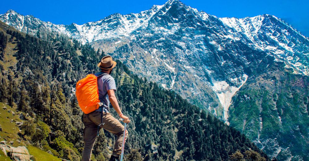 Trip - Man exploring breathtaking mountain scenery with snow-capped peaks under a clear blue sky.