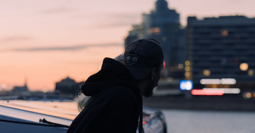 Boat - Man in a hoodie gazes over a city waterfront at sunset, blending urban tranquility.