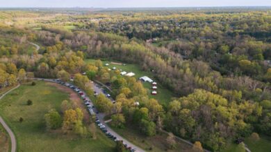 Campsites - Aerial view of a rural campsite surrounded by lush greenery and parked cars.