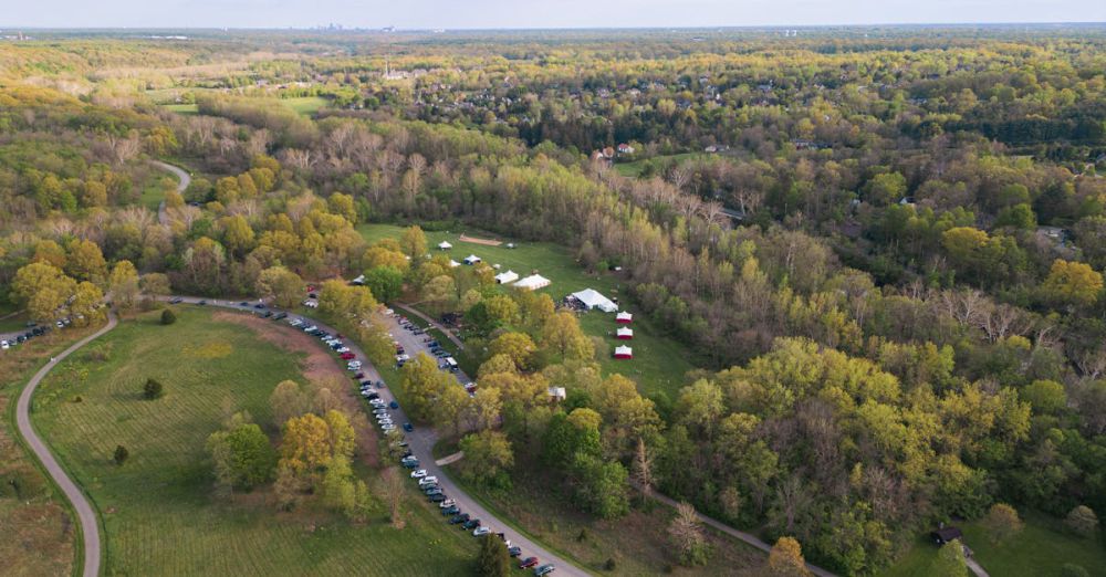 Campsites - Aerial view of a rural campsite surrounded by lush greenery and parked cars.