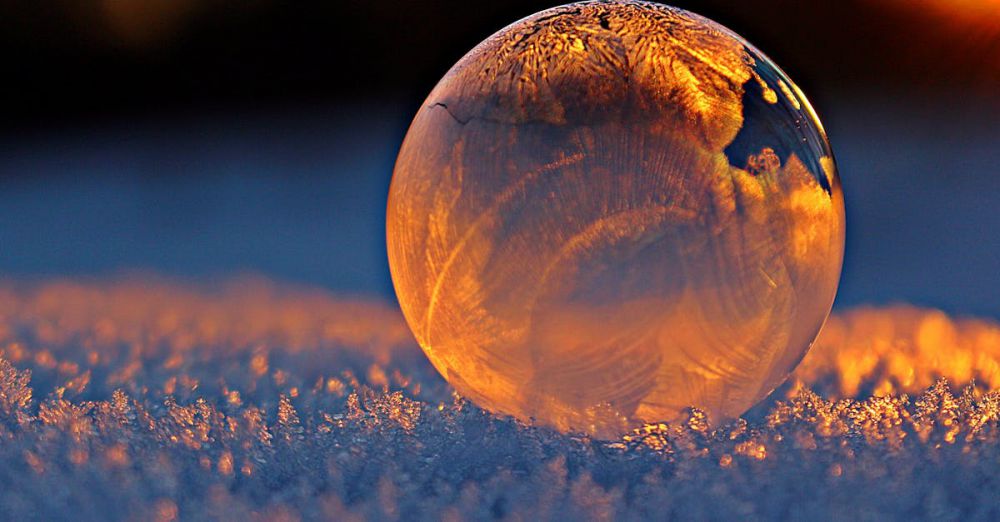 Winter - Close-up shot of a frozen bubble with warm reflections resting on a snowy surface at twilight.