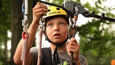 Safety - A young boy enjoying a rope climbing activity outdoors, wearing a helmet and using safety gear.