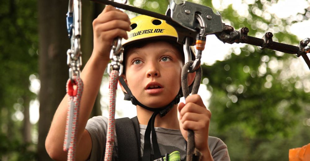 Safety - A young boy enjoying a rope climbing activity outdoors, wearing a helmet and using safety gear.