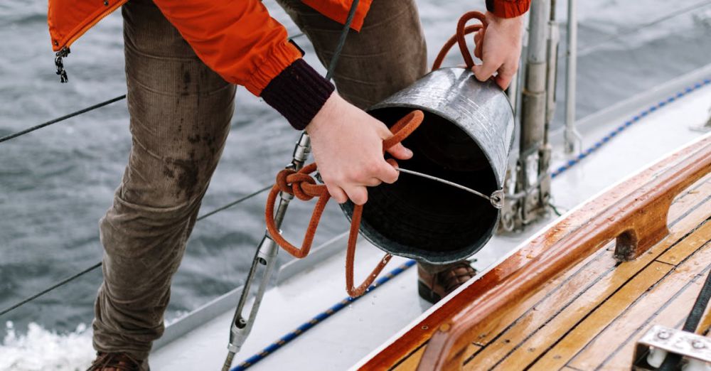 Fishing - Man in orange jacket cleaning sailboat deck with a bucket on the ocean.