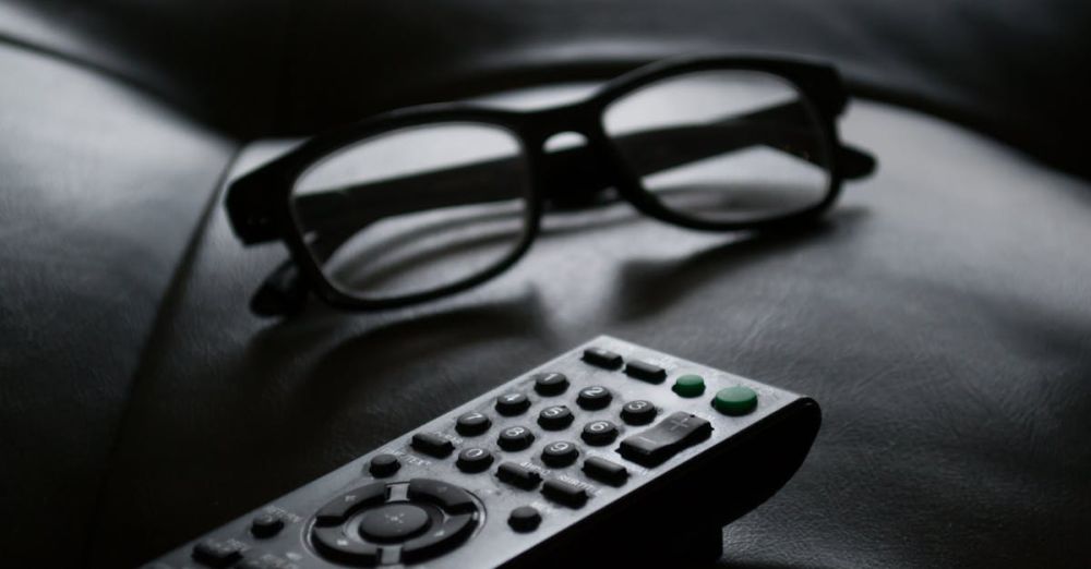 Remote - Close-up of eyewear and a TV remote on a dark leather couch, ideal for home lifestyle themes.