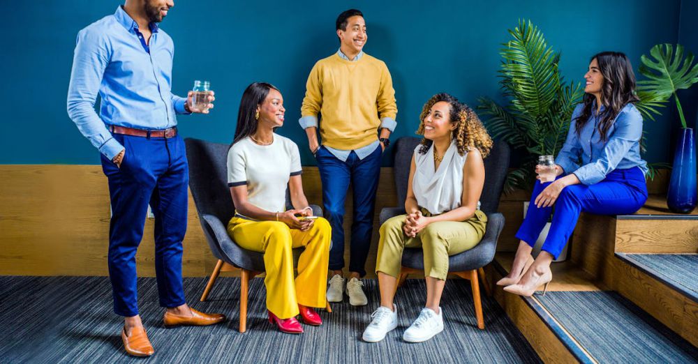 Group - A diverse group of five professionals engaging in a casual indoor meeting, smiling and talking.