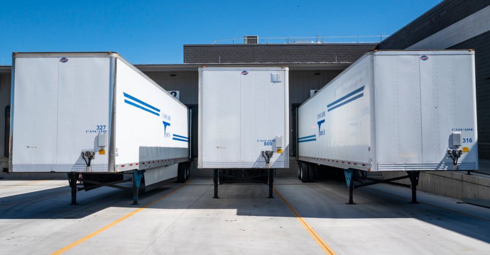 Trailers - Three white cargo trailers parked at an industrial shipping dock under clear blue skies.