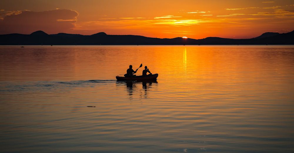 Canoe - Silhouetted canoe with two people rowing on a calm lake at sunset, creating a serene and picturesque scene.