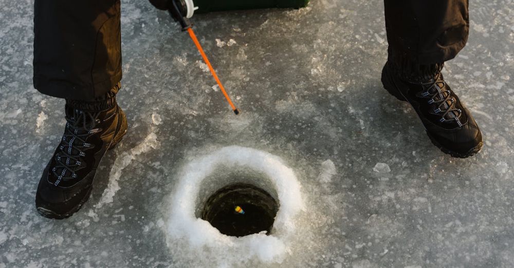 Fishing - Person ice fishing on frozen lake surface with fishing rod and winter boots.