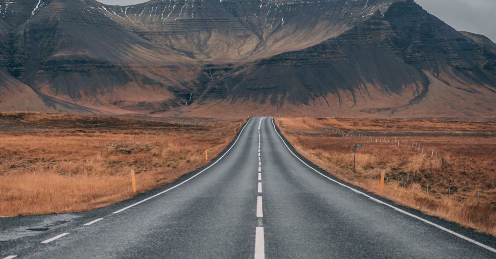 Adventure - A scenic empty road stretches into snow-capped mountains under cloudy skies, offering a sense of adventure and tranquility.