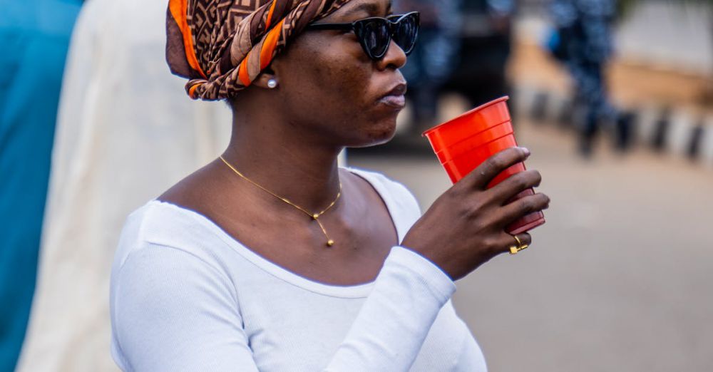 Demonstrations - A Nigerian woman participates in a peaceful protest, holding a red cup and smartphone.