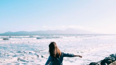 Retreats - A woman freely enjoying the scenic beach view with ocean waves on a sunny day.