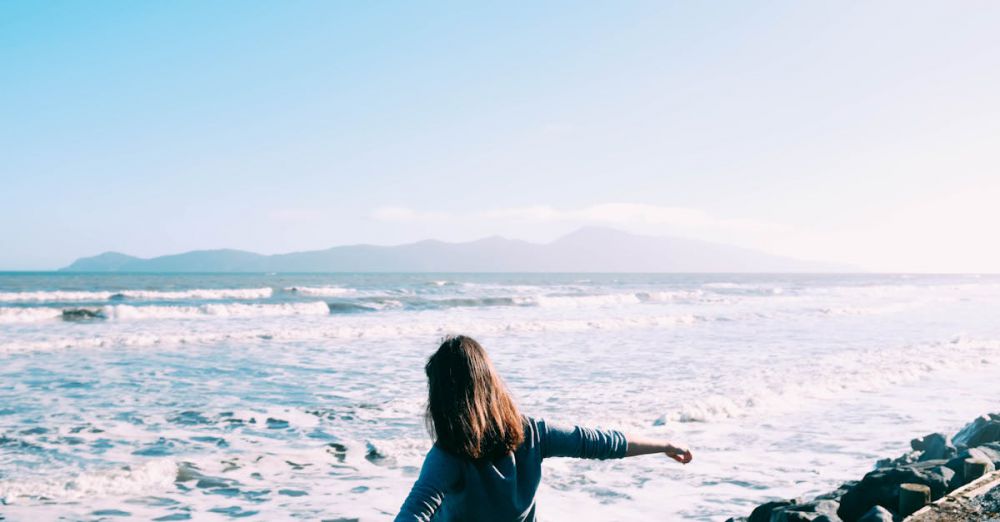 Retreats - A woman freely enjoying the scenic beach view with ocean waves on a sunny day.