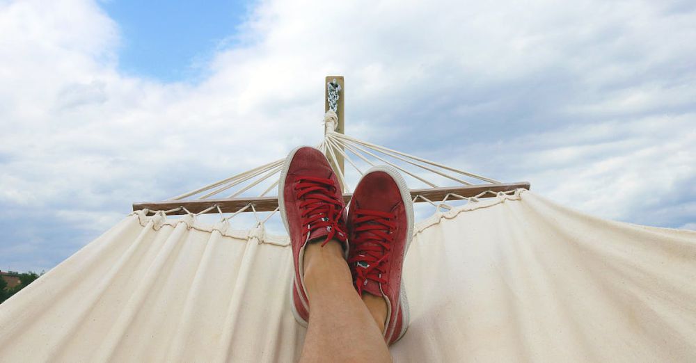 Vacation - Feet resting on a hammock with red sneakers, epitomizing summer relaxation and leisure outdoors.