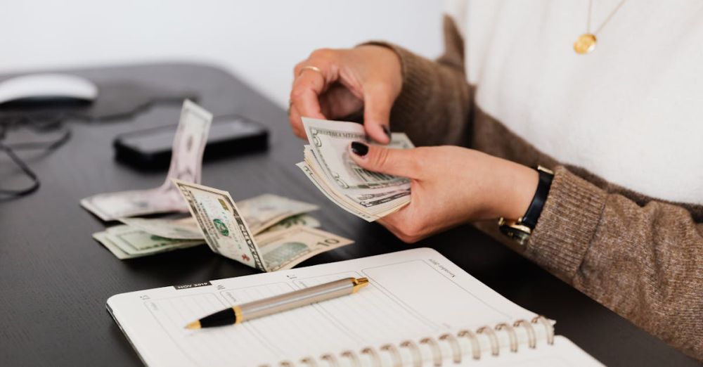 Budget - Close-up of person counting cash with notepad on desk, indicating financial tasks.