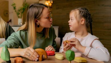 Special Needs - An adult woman and a child with Down syndrome engaging in playful interaction with wooden toys indoors.