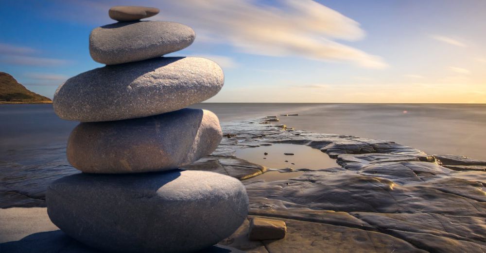 Wellness - A serene stack of stones on the rocky seashore during a peaceful sunrise, embodying balance and zen.